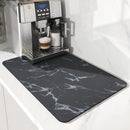 A Lovely Home Icon Coffee Machine Mat—with a black marble pattern, rubber backing, and water-absorbent surface—covers the countertop in front of a coffee machine, providing both stylish décor and practical drainage for your kitchen.