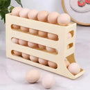 A Lovely Home Icon Refrigerator Egg Storage Box, featuring four layers and an automatic rolling design, neatly organizes brown eggs in the fridge. As one egg is removed, the others roll forward for convenient access. Three eggs are placed outside the plastic beige holder on a marble surface, with a circular art piece visible in the background.