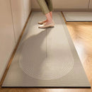 A person stands on the Lovely Home Icon New 1 pc Japanese style soft kitchen diatomite mud floor mat—an easy-to-handle, super absorbent rug with a light hue and geometric stripe pattern, rounding at one end. Only their legs and feet are in view, highlighting the mat’s modern, anti-slip design as it complements the wooden floors and neutral walls.