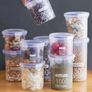 Nine Lovely Home Icon Plastic Sealed Tank Large Capacity Crispers, each labeled with measured capacities, are filled with various dry foods—beans, nuts, seeds, and dried fruit—and neatly stacked on a table while one clear spice container is held above.