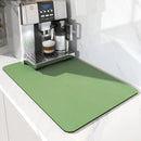 A silver espresso machine rests on the Lovely Home Icon Coffee Machine Mat—a water-absorbent, rubber-backed drying pad in green—adding both style and practical drainage to the white kitchen counter as it prepares a cup of coffee with milk froth, seamlessly doubling as chic home decor.