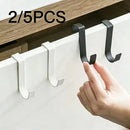 A hand places a black stainless steel Lovely Home Icon Multi-Purpose Hook over a white kitchen cabinet door, alongside two identical white hooks, demonstrating this space-saving hanger for clothes, towels, and more. Text at the top left reads 2/5PCS.