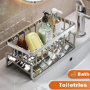 A Lovely Home Icon Sink Cleaning Tools Storage Rack neatly holds bottles, a bar of soap, and a yellow soap dish on a sink. Shiny and rectangular, this multifunctional stainless steel drain rack conveniently organizes toiletries like a sponge holder or kitchen sink organizer. “Bath Toiletries” is labeled at the bottom right corner.