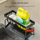 A Lovely Home Icon Sponge Draining Rack – Dishcloth & Dishwashing Liquid Storage, Kitchen Organizer in black metal sits by the sink, holding a towel and a yellow detergent bottle. This waterproof rack features an inclined plastic plate that efficiently drains water straight into the sink below. Informational text highlights the draining function and emphasizes the versatile use of the inclined plate for keeping your kitchen organized.