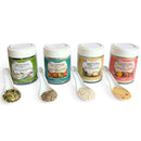 Four jars of SALTOPIA Infused Sea Salts' Saltopia Low Sodium Salad Seasonings, each with a unique label color, are displayed behind ceramic spoons holding samples—a healthy and perfect gift set for salad lovers.