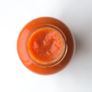 Top view of an open glass jar filled with smooth, orange-red Taycte Famiglia Crispino Basil Tomato Sauce Starter by Taycte, placed on a white background.