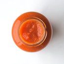 A top-down view of an open glass jar filled with smooth, red-orange Famiglia Crispino Calabrian Chili Pasta Sauce Starter — Peperoncino by Taycte, set against a white background.