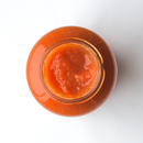 Top view of an open glass jar filled with smooth, orange-red sauce or puree, placed on a white surface. The jar contains Taycte Famiglia Crispino Rustic Pasta Sauce Starter — Slow-Cook Italian Base by Taycte, showcasing its vibrant color and fresh, authentic ingredients.