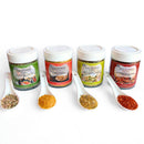 Four jars of SALTOPIA Infused Sea Salts’ Saltopia Low Sodium Seasonings, each with a white sample spoon and green, orange, yellow, or red label, make an ideal gift set for low sodium cooking.