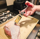 A hand injects marinade into a raw turkey breast using the SpitJack SHOT XL Meat Injector Kit with Deluxe Case and Four Needles by SpitJack, on a tan tray next to a stove in a kitchen.