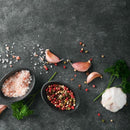 The SALTOPIA Infused Sea Salts SALT SNOBS Gift Set features pink Himalayan salt and mixed peppercorns, showcased with garlic cloves, parsley, and scattered gourmet sea salts and peppercorns on a dark surface.