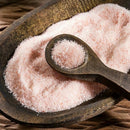 A wooden bowl displays SALTOPIA Infused Sea Salts from the Saltopia SALT SNOBS Gift Set, featuring pink Himalayan salt with a wooden spoon resting on top holding fine, light pink grains.