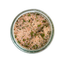 A glass jar of SALTOPIA Infused Sea Salts' Saltopia Salt, Pepper & Garlic seasoning blend—Pink Himalayan sea salt with green herb flakes—viewed from above on a white background.