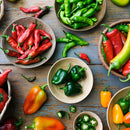 Bowls and baskets of vibrant red, green, yellow, and orange peppers—some whole, some sliced—sit on a rustic table, showcasing their bold flavor enhanced by SALTOPIA Infused Sea Salts' Saltopia Habañero Salt: HOT HEAD.