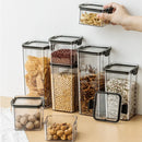 A hand holds a small container above a set of Lovely Home Icon 1-4PCS Sealed Jars Kitchen Organizer Grain Storage Boxes, with the clear, rectangular fresh-keeping containers filled with various dried foods like beans, nuts, and grains on a light surface.