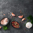 Saltopia Salt, Pepper & Garlic by SALTOPIA Infused Sea Salts is artfully arranged with parsley and garlic on a dark stone background, featuring mixed peppercorns and Himalayan salt for a gourmet touch.