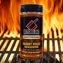 Butcher BBQ Savory Pecan Seasoning bottle on a grill with flames in the background