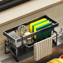 The Lovely Home Icon Sponge Draining Rack – Dishcloth & Dishwashing Liquid Storage, Kitchen Organizer in black is a waterproof, durable plastic rack placed by the sink. It neatly holds green and yellow sponges, a soap dish brush, a scrubber, and features a side hook for hanging a dishcloth—keeping all your essential cleaning items organized and easily accessible.