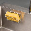 A yellow sponge sits in the Lovely Home Icon Sponge Holder for Kitchen Sink, a stainless steel suction cup caddy mounted to the side of a stainless steel sink.