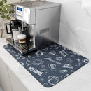 A silver espresso machine brews coffee into a glass cup, which sits atop the Lovely Home Icon Coffee Machine Mat. This water-absorbent dish drying pad features white coffee-themed illustrations and welcoming phrases like “Welcome” and “Enjoy Fresh” on its dark, modern surface with a durable rubber backing. The stylish mat rests on a marble countertop, enhancing the chic atmosphere of the scene.