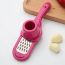A Lovely Home Icon 1PCS Garlic Crusher Press Multi-Functional Manual Ginger Garlic Grinding Grater Cutter, featuring a pink handle and a circular holder, is set next to two garlic cloves on a white surface. In the background, a wooden cutting board holds a red vegetable.
