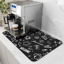 A coffee machine sits on a counter alongside a cup of cappuccino, both resting on the Lovely Home Icon Coffee Machine Mat. This water-absorbent dish drying pad features a rubber backing and eye-catching white illustrations with words like “WELCOME” and “Enjoy Fresh.” The clean counter, adorned with Diatom Mud accents for contemporary style, is complemented by white cabinets in this bright, modern kitchen.