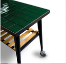 A corner of a WPPO LLC Direct Infinity Side Table Short side 75cm—compatible with Infinity 50 and 66—featuring a glossy green tiled top, black metal legs, a wooden slat shelf beneath, and a wheel on one leg, set against a white background.