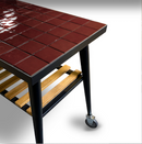 The WPPO Infinity Side Table Short side 75cm by WPPO LLC Direct features a glossy, dark red tiled top and sturdy black metal legs. Designed to fit Infinity 50 and 66, this striking side table offers a lower wooden slatted shelf for additional storage, while a wheel on one leg adds both charm and mobility.