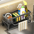 The Lovely Home Icon Multifunctional Sponge Draining Rack – Kitchen Cloth & Dishwashing Liquid Storage, Sink & Kitchen Organizer holds cleaning supplies, sponges, a brush, spray bottles, and dish soap on the kitchen counter, with a checkered towel hanging from the front.