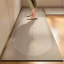 A person wearing light shoes and olive-green pants stands on the Lovely Home Icon New 1 pc Japanese style soft kitchen diatomite mud floor mat, featuring a modern beige design with a rounded end and thin white curved lines. The super anti-slip, super absorbent mat is placed on a wooden floor near a wall, with another matching carpet visible in the background.