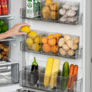 A hand places a lemon on a refrigerator door organized with Lovely Home Icon 1PCS Refrigerator Side Door Storage Box Food Vegetable Fruit Eggs Fresh Organizer, neatly storing lemons, oranges, eggs, garlic, corn, carrots, cucumber, and eggplant.