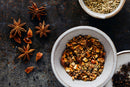 Overhead view of a bowl containing World Spice Seattle Salmon Rub, featuring roasted spices, surrounded by star anise, fennel seeds in another small bowl, and scattered spices on a dark textured surface.