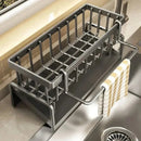 The Lovely Home Icon Multifunctional Sponge Draining Rack – Kitchen Cloth & Dishwashing Liquid Storage, Sink & Kitchen Organizer sits beside the sink, its side bar holding a striped towel. This waterproof rack, empty for now, rests on the countertop near a window—an ideal organizer for those looking to keep their kitchen essentials tidy.