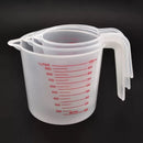 Three transparent plastic measuring cups from Lovely Home Icon, with red PVC scale markings and handles, are stacked together against a black background; each cup measures volumes of 250ml, 500ml, or 1000ml, making them the perfect kitchen baking tools for all your cooking needs.
