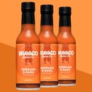 Three bottles of Bravado Spice Serrano & Basil Hot Sauce by Bravado Spice, a medium-heat Italian-inspired hot sauce ideal for drizzling on pizza, are displayed against an orange background. The bottles feature black caps and orange labels with white text.