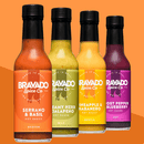 Four bottles of Bravado Spice hot sauces are displayed in a row, each delivering a distinct botanical heat. Flavors from left to right: Bravado Spice Serrano & Basil Hot Sauce—ideal as an Italian-style hot sauce or pizza drizzle—Creamy Herb & Jalapeno, Pineapple & Habanero, and Ghost Pepper & Blueberry.