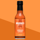 A bottle of Bravado Spice Serrano & Basil Hot Sauce by Bravado Spice, with an orange label indicating its flavor and medium heat level, set against a geometric orange background—an Italian-inspired hot sauce delivering botanical heat, perfect for drizzling on pizza.