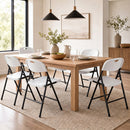 Modern dining room featuring a wooden table, DirectDeals Foldable Plastic Dining Chairs Set of 6 with Ergonomic Backrest, pendant lights, minimal decor, vases with greenery, neutral wall art, and sunlight from a large window.