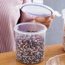 A person opens the Lovely Home Icon Plastic Sealed Tank Large Capacity Crisper Kitchen Organize Grain Storage Box with Scale, a clear airtight container filled with a mix of grains, beans, and seeds, on a wooden surface.