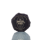 A round bar of The Immaculate Beard Dark Shave Soap Puck, wrapped in black, is crafted as a natural shave soap with kaolin clay for sensitive skin. Labeled with scent notes of tobacco blossom, caramel, honey, and rose, this 3 oz (85 g) soap puck reflects elegantly on a white surface.