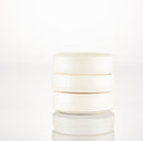 Three stacked, round, white ceramic Shave Bowls by The Immaculate Beard—perfectly crafted for your favorite shave soap puck—are arranged at the center of a glossy, reflective surface set against a plain white background.
