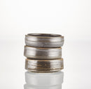 Three stacked, round ceramic Shave Bowls by The Immaculate Beard, featuring a matte brown and gray finish, are displayed against a plain white background with a subtle reflection at the base—ideal for creating a rich, moisturizing lather with your favorite shave soap puck.