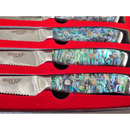 The BBQ Boards® BBQ Blades™ Steak Knife Set features three serrated steak knives with iridescent, multi-colored handles in a red-lined case. Reflective blades labeled BBQ Blades™ enhance this premium, decorative set.