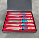 The BBQ Boards® BBQ Blades™ Steak Knife Set comes in a black box with a red interior, featuring six serrated steak knives with silver blades and handles crafted from wood and turquoise resin.