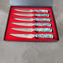 The BBQ Boards® BBQ Blades™ Steak Knife Set includes six serrated steak knives with colorful, abalone shell-patterned handles, all arranged in a sleek black box with a bold red insert.