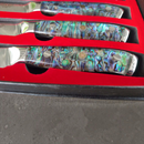 The BBQ Boards® BBQ Blades™ Steak Knife Set features three premium steak knives with iridescent abalone-patterned handles, displayed in a black case with red lining, each knife resting in its own slot.