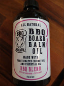 A bottle of BBQ Board Balm® Care Pair Oil by BBQ Boards® rests on wood. This all-natural conditioner, made with fractionated coconut oil and essential oils, features a signature BBQ blend with cinnamon and peppermint for premium cutting board care.