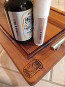 The BBQ Boards® wooden cutting board is shown with two BBQ Board Balm® Care Pair Wax and Oil bottles on top, all placed on a tiled countertop—perfect for caring for your board.