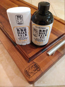BBQ Boards® BBQ Board Balm® Care Pair Wax and Oil in Orange scent, ideal for cutting board care, shown on a branded wooden cutting board with a metal handle.