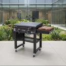 A BBQ Boards® 30" Blackstone Griddle Side Cutting Board is attached to a sleek black outdoor grill on a modern patio with large windows and lush greenery in the background.